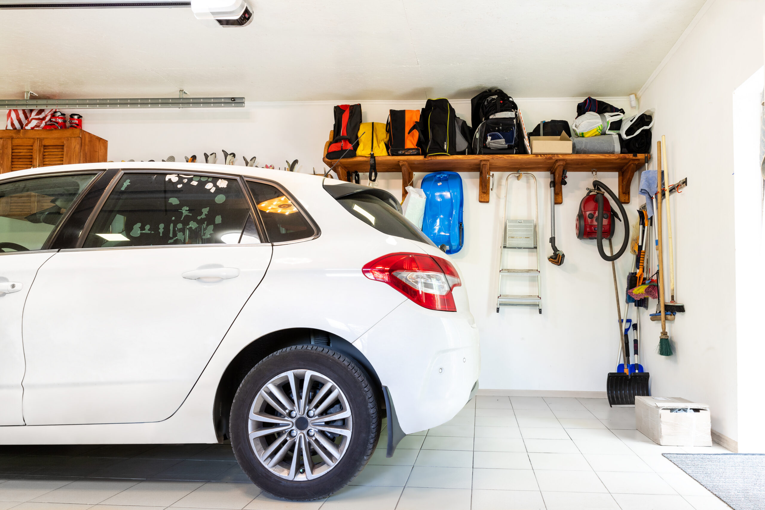 Home suburban car garage interior with wooden shelf , tools and equipment stuff storage warehouse on white wall indoors. Vehicle parked at house parking background.