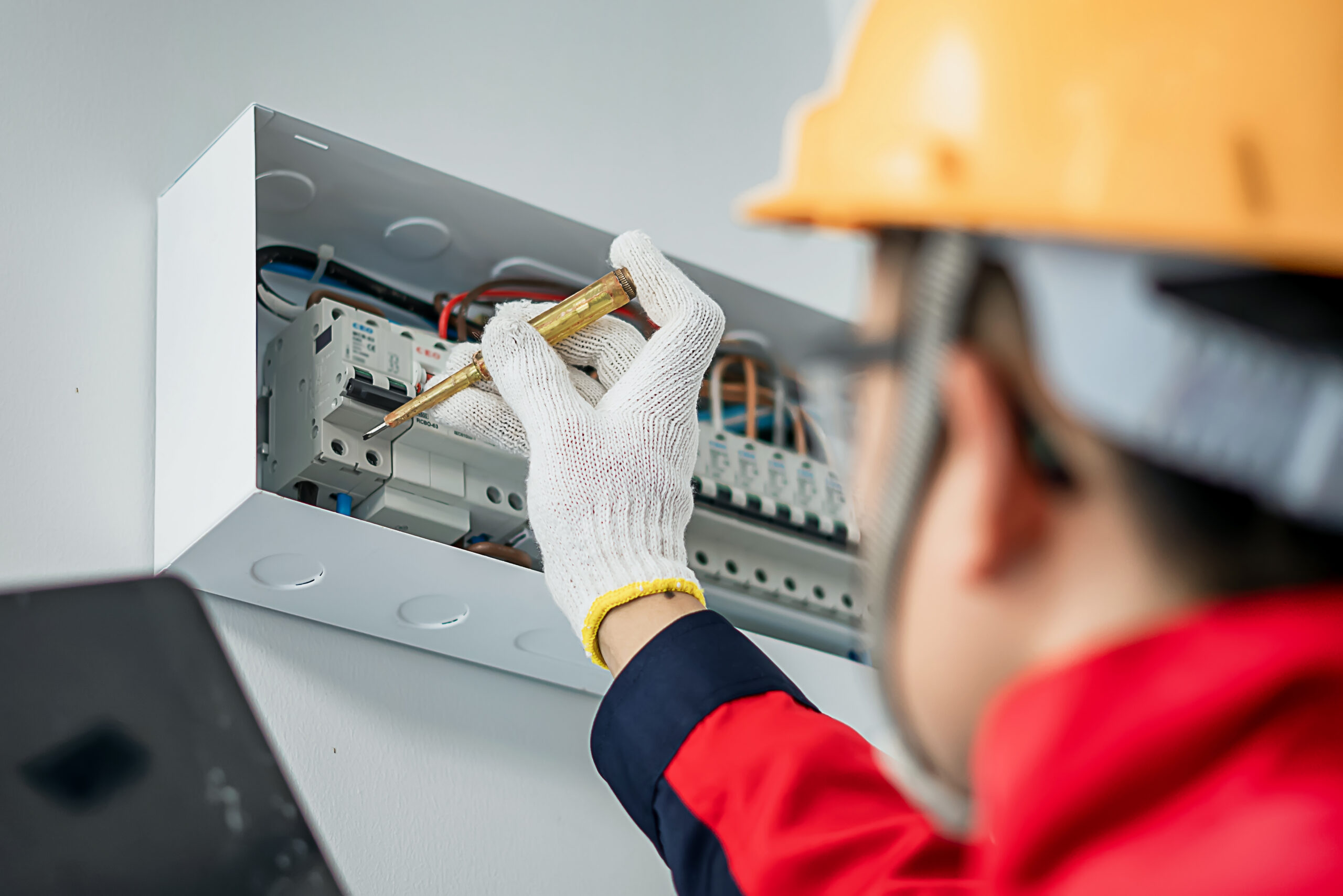 electrical engineer wearing safety helmet inspecting home electrical system with tools and tablet at indoor building site